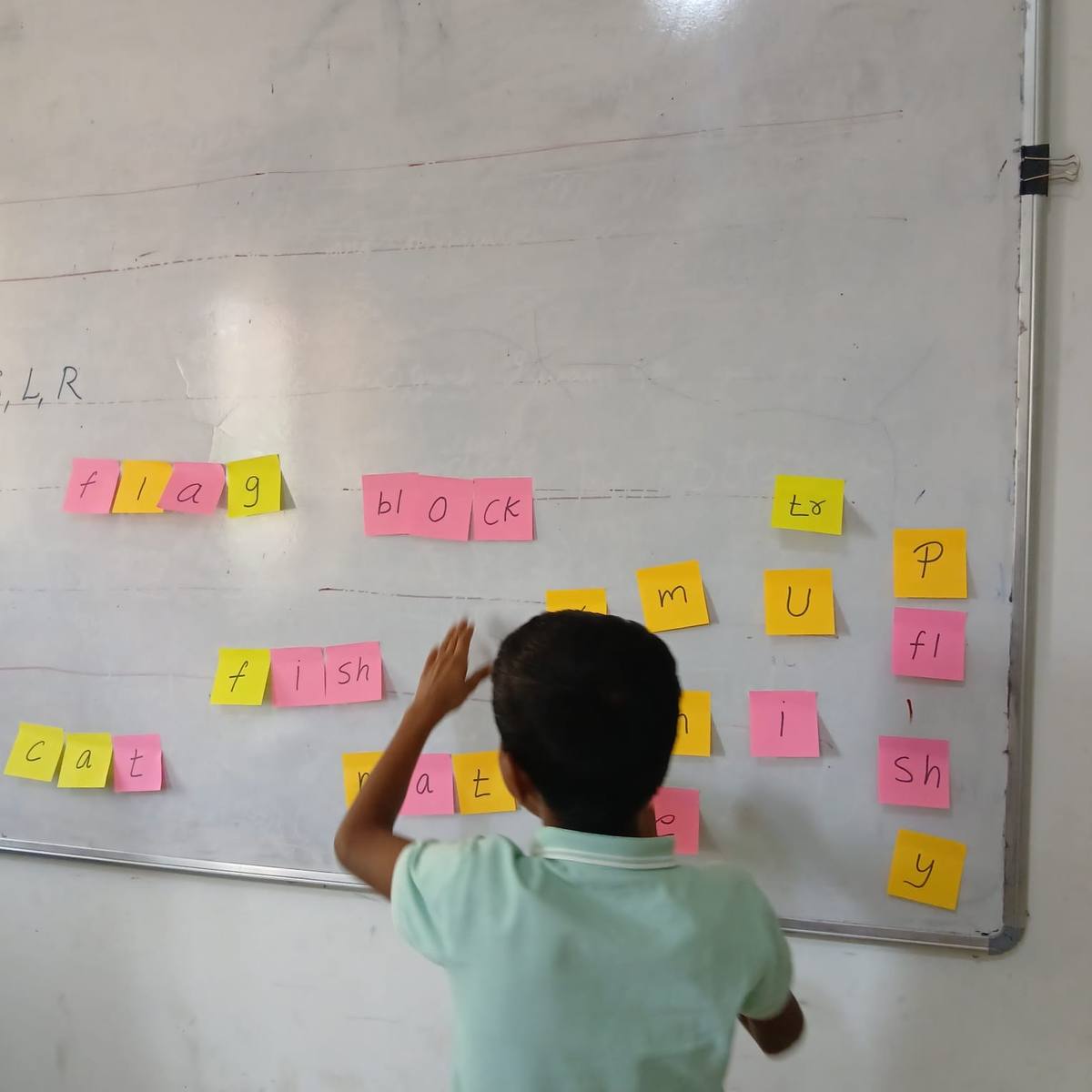 A student building words with sticky notes on the whiteboard during a phonics activity.